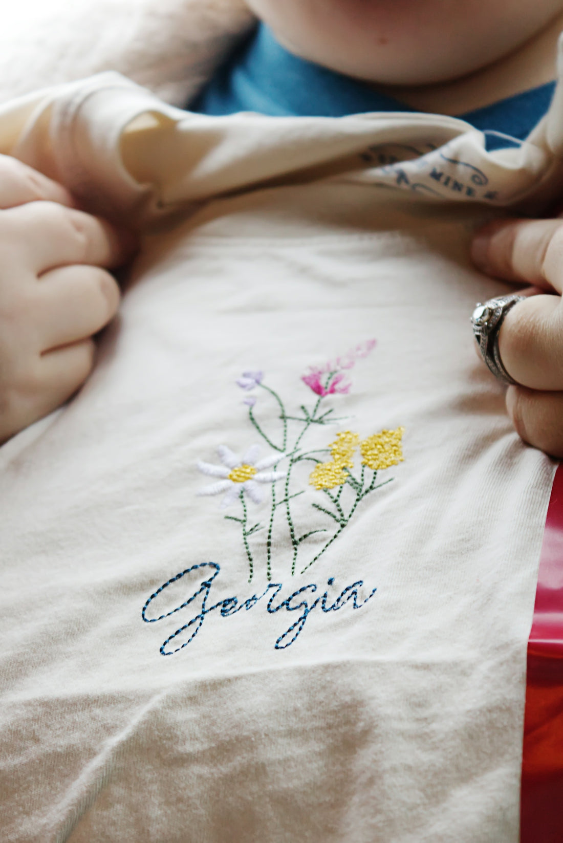 A baby is holding onto a t - shirt with flowers on it